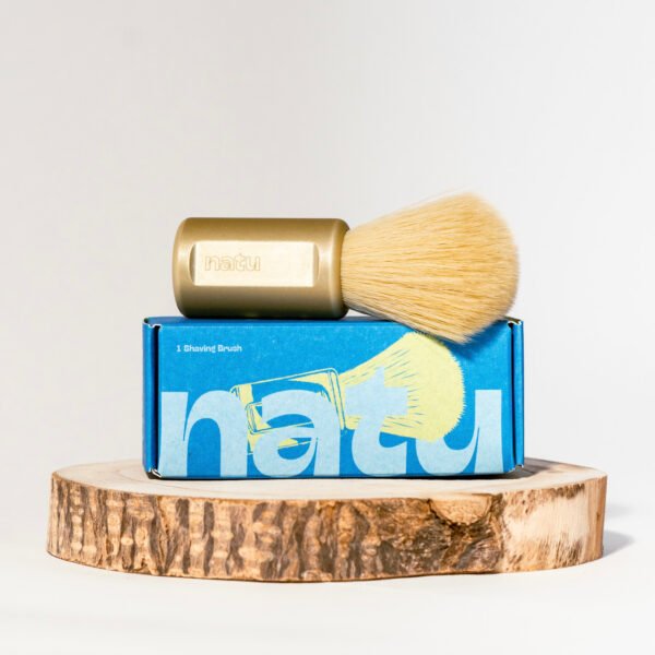 NATU synthetic shaving brush in gold resting on its retail box
